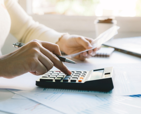 Side view of a woman in yellow shirt using a calculator while doing taxes