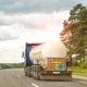 Back View Of A Semitruck Driving Down The Road With Cloudy Sky In The Background