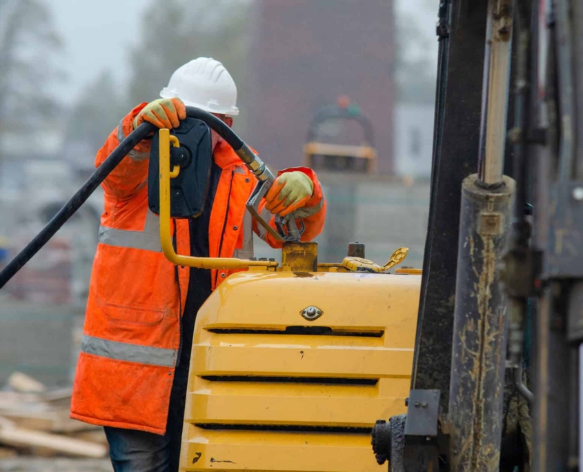 Construction-worker-in-safety-gloovs-filling-excavator-with-diesel-fuel-on-building-site Construction Worker In Safety Gloovs Filling Excavator With Diesel Fuel On Building Site