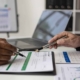 Side View Of Two People Filling Out Financial Doucments At Desk
